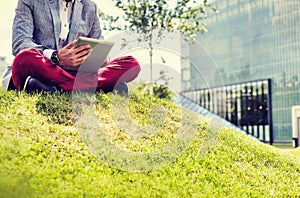 Portrait of young attractive businessman using digital tablet while sitting on the grass