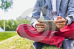 Portrait of young attractive businessman using digital tablet while sitting on the grass