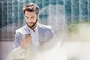 Portrait of young attractive businessman using smartphone with earphones on