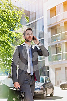 Portrait of young attractive businessman walking while talking on smartphone