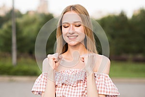Portrait of a young and attractive Caucasian blonde girl with closed eyes. The girl showing a gesture of victory. Success, achieve