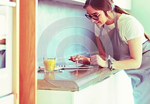 Portrait of young attractive caucasian brunette housewife at kitchen. Morning with cup of coffee and tablet pc