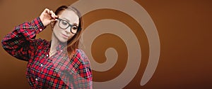Portrait of a young attractive Caucasian woman in a red shirt and glasses on a brown background. Advertising glasses for