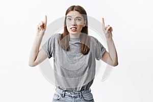 Portrait of young attractive dark-haired female student in fashionable outfit making funny face expression, pointing