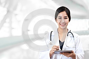 Portrait of young attractive female asian doctor or physician smiling and holding tablet and stethoscope medical equipment looking