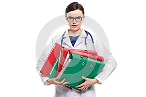 Angry young woman doctor with stethoscope holding binders in her hands in white uniform on white background