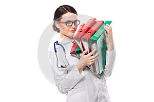 Angry young woman doctor with stethoscope holding binders in her hands in white uniform on white background