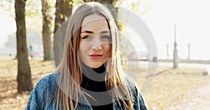 Portrait of young attractive female who smiling and looking at the camera on autumn park. Cheerfully pretty woman at