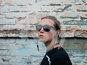 Portrait of young attractive girl in black t-shirt and sunglasses in rock style on urban background listening to music