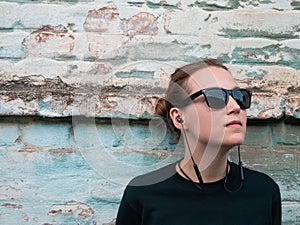 Portrait of young attractive girl in black t-shirt and sunglasses in rock style on urban background listening to music