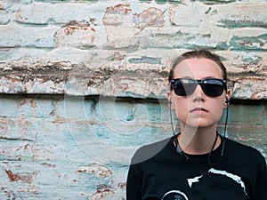 Portrait of young attractive girl in black t-shirt and sunglasses in rock style on urban background listening to music