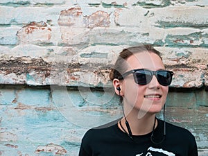 Portrait of young attractive girl in black t-shirt and sunglasses in rock style on urban background listening to music