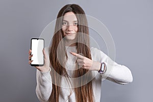 Portrait of a young attractive girl woman with dark long hair easily smiling and points a finger at a blank cell phone smartphone