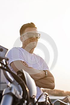 Portrait of a young attractive guy in sunglasses. Nice young man in a white T-shirt and black jeans on a motorcycle. Life style