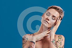 Portrait of a young attractive half naked tattooed woman with perfect skin closing eyes, gesturing sleeping isolated