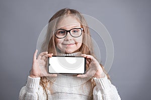 Portrait of a young attractive little girl with blond long flowing hair in a white sweater hold shows a mobile phone with a white