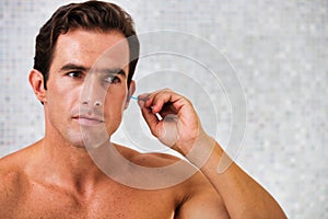 Portrait of young attractive man cleaning his ears with cotton buds in the bathroom