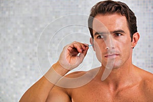 Portrait of young attractive man cleaning his ears with cotton buds in the bathroom