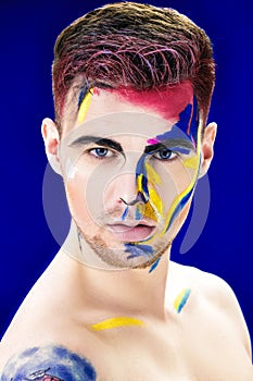 Portrait of young attractive man with colored face paint on blue background. Professional Makeup Fashion. ffantasy art