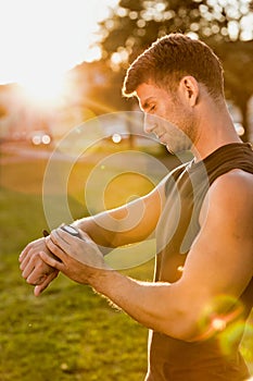 Portrait of young attractive man looking at his wristwatch in park with lens flare
