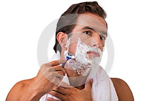 Portrait of young attractive man shaving his beard while looking in the mirror