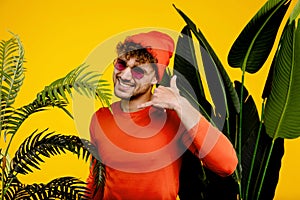 Portrait of young attractive man showing aloha gesture, isolated yellow background with green plants