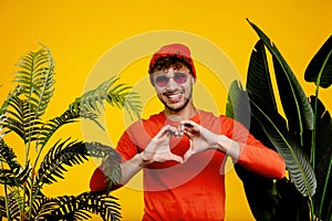 Portrait of young attractive man showing heart with his hands , love concept on yellow background with green plants