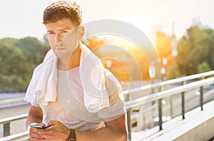 Portrait of young attractive man standing with towel on his shoulders while using smartphone