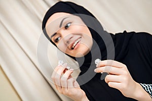 Portrait of a young and attractive muslim woman in a turban or hijab listening to streaming music on her smartphone.