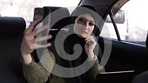 Portrait of a young, attractive muslim woman wearing a hijab commuting in a car. She is wearing a dark clothes, sitting