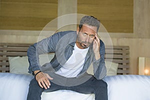 Portrait of young attractive overwhelmed and depressed man sitting on bed worried and frustrated suffering depression crisis fired