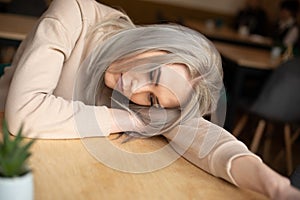 Portrait of young attractive pensive woman with long grey hair with make-up in sweatshirt laying head on hand on table.