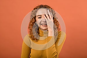 Portrait of a young and attractive, pleased and laughing redhead Caucasian girl in an orange jumper isolated on an orange studio b