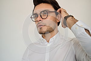 Portrait of young attractive serious brunette man in white shirt and eyeglasses thoughtfully looking aside over white