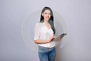 Portrait of young attractive smiling woman holding tabled against gray background