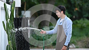 Portrait of young attractive spraying water from hose watering a plant.