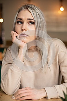 Portrait of young attractive thoughtful woman with long grey hair with cute professional make-up resting chin on hand.