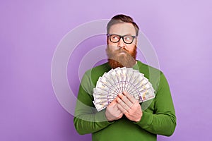 Portrait of young attractive wealthy male brainstorming hold lots of money fan of dollars isolated on purple color