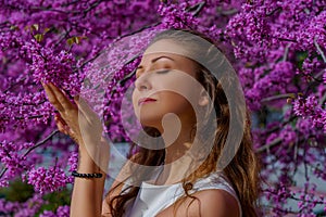 Portrait of young attractive woman with brown hair poses tender in blossom pink tree