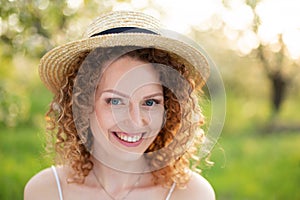 Portrait young attractive woman with curly hair in a stylish wicker hat in a green garden