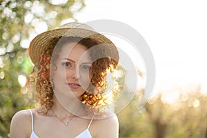 Portrait young attractive woman with curly hair in a stylish wicker hat in a green garden