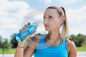 Portrait of young attractive woman drinking energy drink in park