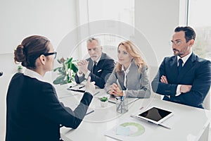 Portrait of young attractive woman in glasses having job interview with three stylish business persons in financial