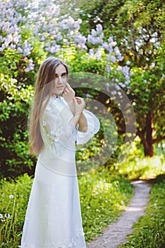 Portrait of young attractive woman in long white wedding dress in spring garden with blooming trees. Spring background.