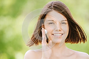 Portrait of young attractive woman putting cream on her face