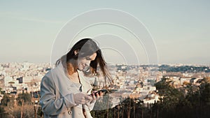 Portrait of young attractive woman standing at the panorama of Rome, Italy. Female use the smartphone outside.
