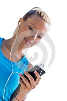 Portrait of young attractive woman standing while using and listening to music on her smartphone in park