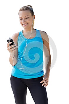 Portrait of young attractive woman standing while using and listening to music on her smartphone in park