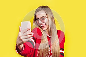 Portrait of a young attractive woman in sunglasses making selfie photo on smartphone isolated on a yellow background