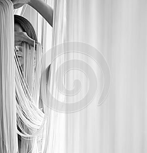 Portrait of a young attractive woman with uncovered shoulders decoratively pulling the threads of a string curtain with hands